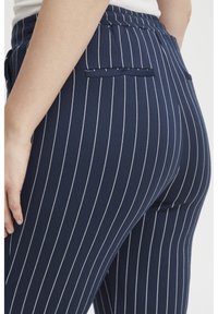 Navy blue striped pants with a smooth texture, featuring thin white vertical stripes, side pockets, and a fitted design.