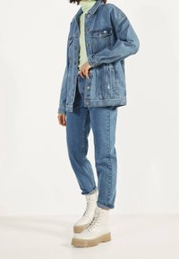 Ljusblå denimjacka med avslappnad passform, framfickor och knäppning. Sammanställd med högmidjade blå jeans och vita platåstövlar.