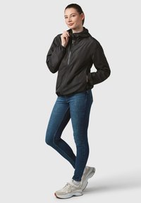 Black lightweight zip-up jacket with a hood, featuring long sleeves and a fitted design, paired with blue jeans and light sneakers.