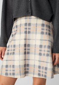 Gonna a quadri in un morbido tessuto leggero con colori beige, grigio e pesco. Forma svasata con una texture liscia e una leggera lucentezza.