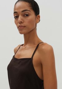 Schwarzes ärmelloses Top aus strukturiertem Material, mit dünnen Trägern und quadratischem Ausschnitt, das ein tailliertes Design mit minimalen Details betont.