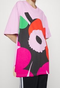 Camiseta de algodón rosa con corte holgado y un gráfico de frutas llamativo en rojo, verde y negro. Mangas cortas, cuello redondo y textura suave.