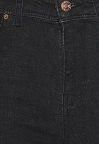 Os jeans de denim pretos apresentam uma textura suave, botão de cobre e detalhes costurados. O design inclui uma cintura ajustada e corte reto nas pernas.