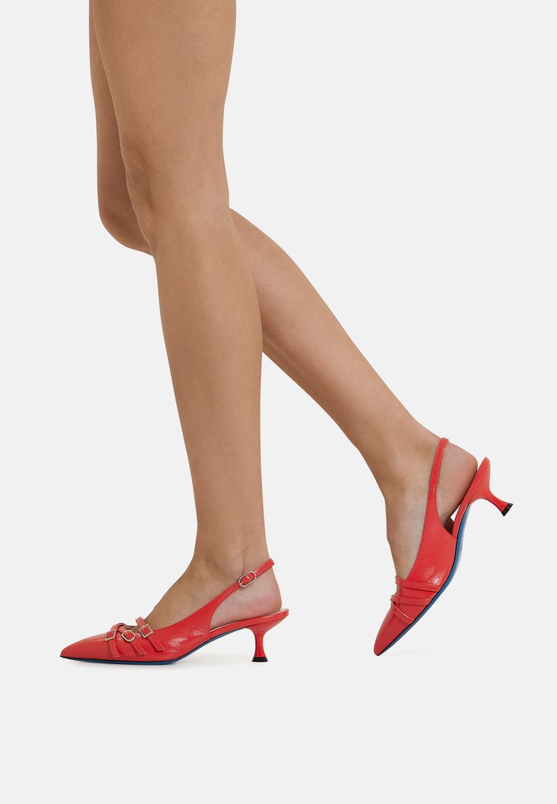 Decollete slingback in pelle rossa con punta affusolata, tacco piccolo e dettagli di cinturini con accenti in tono oro. Superficie strutturata e soletta interna in contrasto.
