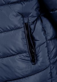 Marine pufferjack sectie met gestikte quiltpatroon en een zwarte ritszak aan de linkerkant met strakke hardwaredetails.