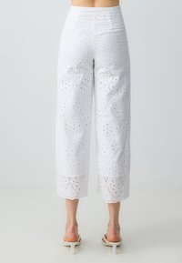 Witte cropped broek met intrigerende oogjes borduurwerk, gekartelde zoom en textuurstof. Kenmerkt zich door een hoge taille en wijd uitlopende pasvorm.