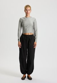 Grå langærmet crop top med buet sømdetalje, parret med løstsiddende sorte bukser og sorte mesh-flade sko. Enkel, afslappet design.