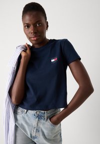 Marineblå bomulds T-shirt med cropped pasform, der har et lille logo i rød, hvid og blå, parret med lyse, vaskede denimjeans.