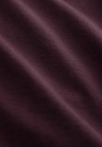 Textilprov i djup burgundy med en slät, något glansig yta, som har subtila ribbningar och draperingsdetaljer.