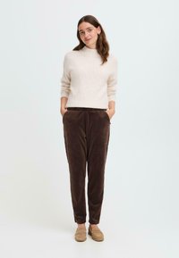 Cream-colored knitted sweater with a high neckline paired with brown corduroy tapered pants, featuring side pockets and soft texture.