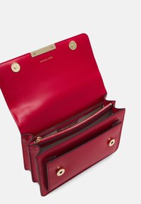 Czerwona skórzana torebka z złotymi elementami, posiadająca zasuwaną kieszeń oraz dwa zapięcia na zatrzask, zaprojektowana w strukturalnym kształcie.