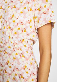 Robe rose clair avec un motif floral dans des nuances blanches, jaunes et oranges. Les manches courtes et le tissu texturé créent une apparence douce.