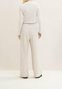 Jasnoszary, prążkowany top z długim rękawem i falbaniastym dołem, w połączeniu z szerokimi, jasnoszarymi spodniami. Oba elementy mają miękką teksturę.