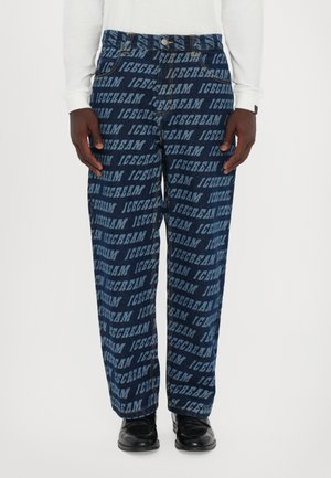 Denim pants in dark blue with repeated "ICECREAM" text pattern in lighter blue. Loose fit with standard pockets, worn with black shoes.