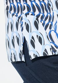Kurzarmhemd mit einem blauen und schwarzen abstrakten Muster auf weißem Hintergrund, mit seitlichen Schlitzern und einem geraden Saum. Kombiniert mit dunkler Denim.