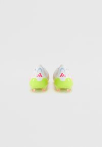Botas de fútbol blancas con acentos en rosa y azul, que cuentan con una suela de color verde brillante. Parte superior texturizada para agarre y soporte, con tacos transparentes.