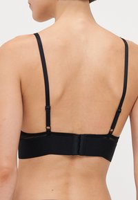 Black bra with adjustable straps, featuring a smooth fabric and hook-and-eye closure. Minimalist design with sleek lines and no visible embellishments.