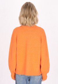 Maglione arancione oversize con polsini e orlo a costine, realizzato in materiale morbido. Stilizzato con spalle rilassate e design posteriore.