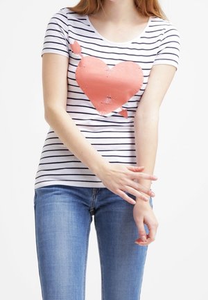 T-shirt bianco a maniche corte con strisce orizzontali nere e una grafica di un cuore corallo usurato al centro. Abbinato a jeans azzurri.