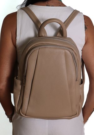 Sac à dos en cuir beige avec deux compartiments zippés, une poignée supérieure arrondie et des bretelles réglables. Surface texturée avec des accents minimaux.