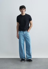 Černé tričko s krátkými rukávy s reliéfním nápisem, spojené se světle modrými džínami širokých nohavic a černými teniskami. Jednoduchý a ležérní outfit.