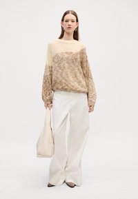 Strikkegenser i beige og krem med gradientdesign; kombinert med kremfargede vide bukser og en beige toteveske. Enkle øredobber fullfører antrekket.