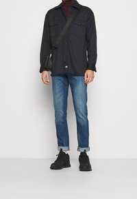 Černá košile na knoflíky s dvěma náprsními kapsami, spárovaná s denimovými džíny. Otočené manžety, tmavé tenisky a malá černá kabelka přes rameno.