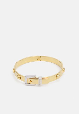 Pulsera de metal dorado con un acabado suave, que presenta tachuelas redondas y una correa de hebilla en tono plateado. Diseñada en forma circular.