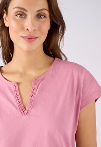 Top corto de manga corta color rosa claro con escote redondeado, adornado con encaje. El material es suave y tiene una textura lisa.