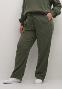 Olivgrüne, leichte Stoffe, weit geschnittene Hosen mit strukturierter Oberfläche. Mit einem elastischen Bund und Kordelzug sowie seitlichen Taschen.
