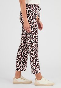 Pantaloni neri con un motivo ondulato bianco e rosso, dotati di vita con cordino e vestibilità affusolata, abbinati a sneakers di colore chiaro.