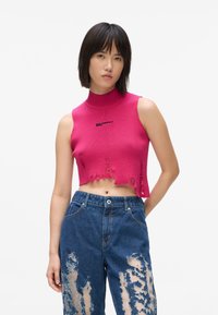 Fukšijas krāsas piegrieztais bez piedurknēm džemperis ar ribotu tekstūru, augstu kaklu un nodilušu malām. Apvienots ar ziliem plecu izšuvumiem denimi džinsiem, kas ir izraizīti.