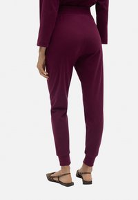 Pantalones jogger burdeos con un corte ajustado, cinturilla elástica y puños acanalados, fabricados en tejido suave. Las costuras visibles añaden detalle.