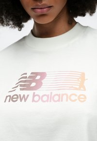 Svetlozelené bavlnené tričko s prechodom ružovej a oranžovej farby s logom "New Balance" a siluetou bežca v pohybe.
