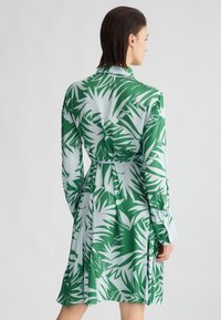 Abito verde e azzurro chiaro con un motivo a foglia, maniche lunghe, vita cintrata e una silhouette fluttuante. Tessuto dalla consistenza liscia.