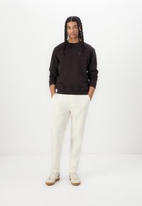 Sort sweatshirt med rund halskrave, parret med off-white bukser og beige sneakers. Modellen har lange fletninger. Minimalistisk stil.