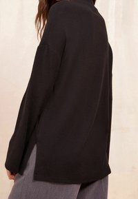 Musta pitkähihainen paita, jossa on löysä istuvuus, sivureiät ja pehmeä rakenne. Suunniteltu korkealla kauluksella ja pudotetuilla harteilla.