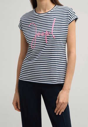Vrouw draagt een blauw-wit horizontaal gestreept shirt met korte mouwen en roze geborduurde tekst "joop!" en effen blauwe broek.