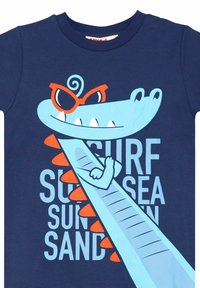 Marineblaue Baumwoll-T-Shirt mit einem Cartoon-Krokodil, das orangefarbene Sonnenbrille und Stacheln trägt, begleitet von dem Text "SURF SUN SEA SAND".