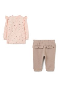 Vestido rosa de manga larga con pequeños puntos rojos y grises y detalles de volantes en los hombros, combinado con pantalones beige acanalados que tienen una cinturilla con volantes.