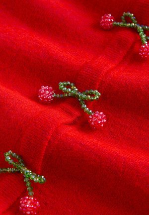 Punane villakangas, millel on rohelised helmestest aksessuaarid, mis on kujundatud nagu paelad ja väikesed lillekesed, läikiva tekstuuriga, lisades dekoratiivset detaili.
