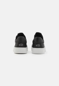 Baskets en cuir noir avec semelles en caoutchouc blanc, présentant une texture lisse et le logo GANT sur le talon. Design simple, style bas.