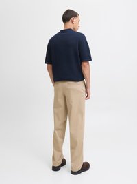 Námornícky krátky rukáv polo tričko v kombinácii s béžovými nohavicami a tmavými topánkami. Polo tričko má štruktúrovanú tkaninu a klasický dizajn goliera.