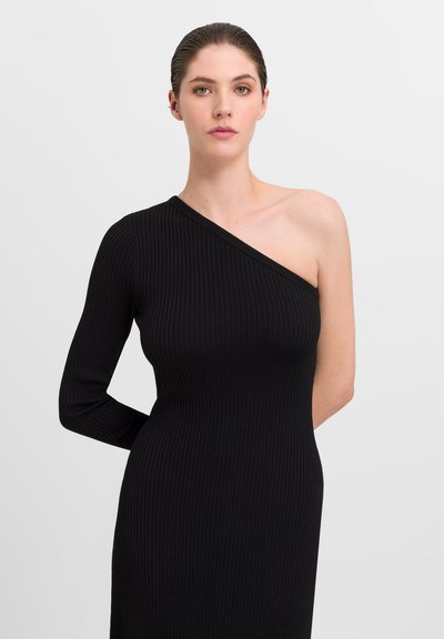 Robe noire asymétrique à côtes avec une manche longue et un côté dénudé. Texture lisse et silhouette ajustée.