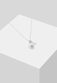 Sudirta sudraba kulonu kaklarota ar kuģa riteņa un āķa piekariņu, ar izsmalcinātu apdari un trauslu ķēdīti.