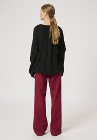 Sort, textured sweater med løs pasform og diamantmønster, parret med brede bordeaux bukser. Set fra ryggen.