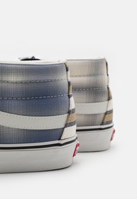 Hochformat Sneaker mit einem strukturierten Textil-Obermaterial in Blau, Beige und weißen Mustern. Merkmale kontrastierende weiße Akzente und eine Gummisohle.