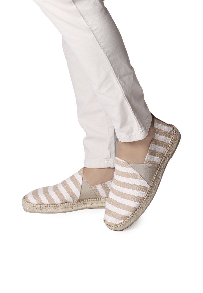 Ribadest vöödiga espadrillid, millel on beež ja valge kangas, elastsed külgpaneelid ja jute köitest kant. Kanda valgete pükstega.