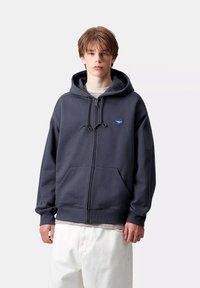 Felpa con zip blu navy realizzata in morbido cotone, dotata di tasca a marsupio, cappuccio con cordino e un piccolo logo a forma di cuore sul petto.