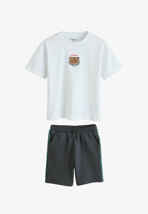 Hvid T-shirt med korte ærmer med et lille tigeransigt og teksten "WILD ONE", kombineret med sorte shorts med snøre og sidelommer med striber.